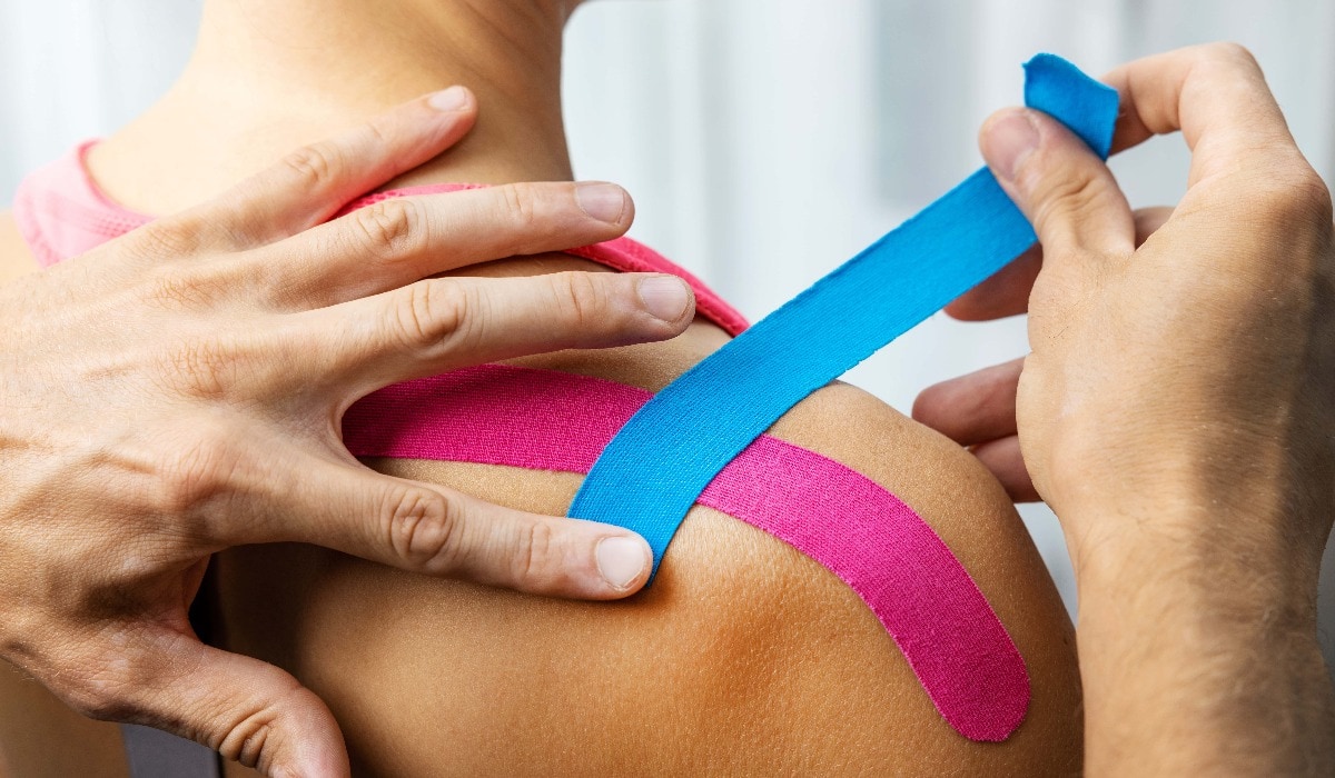 kinesiotaping - physiotherapist taping injured patient shoulder with kinesio tape after muscle injury