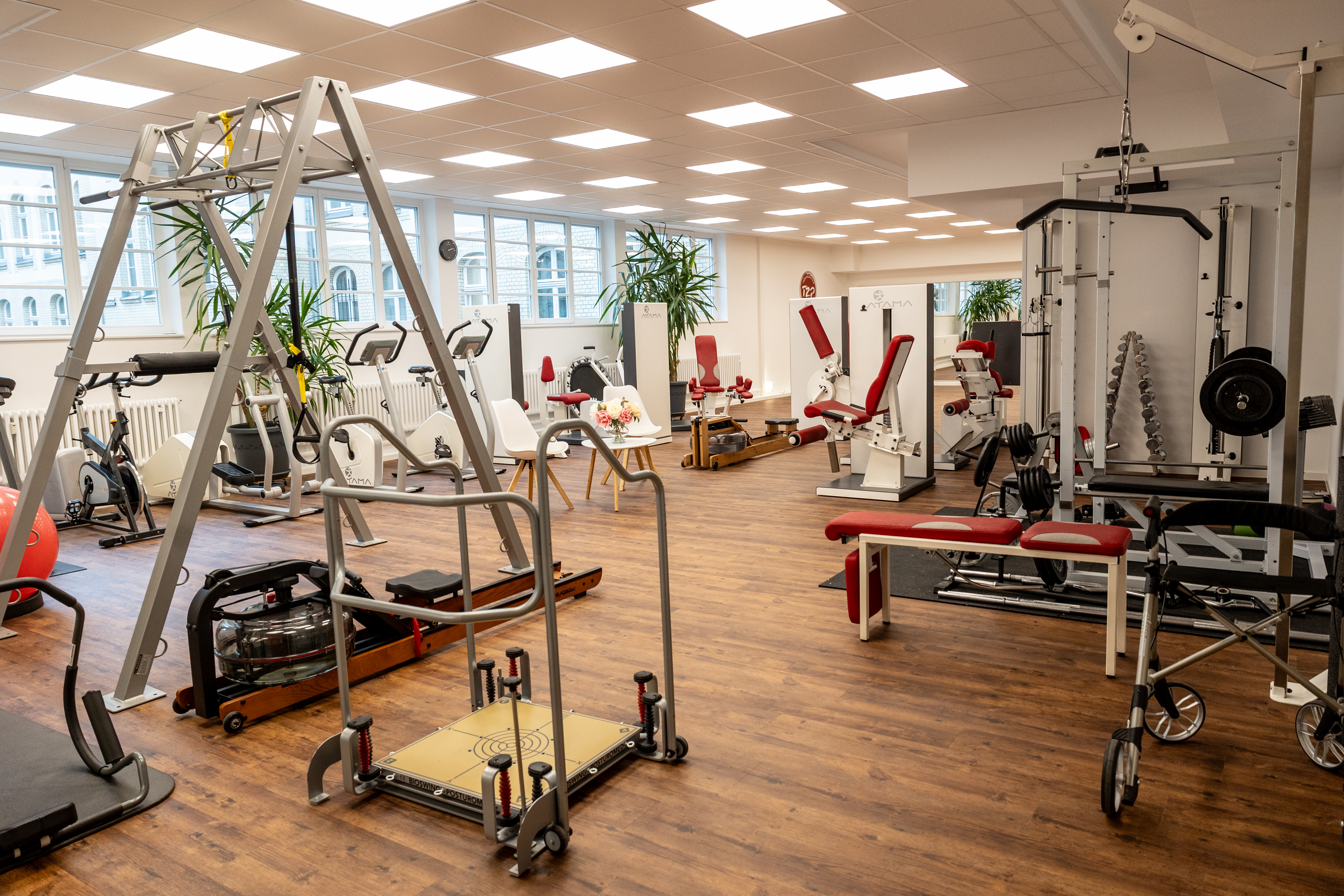 Ein heller Fitnessraum mit roten und weißen Geräten und großen Fenstern