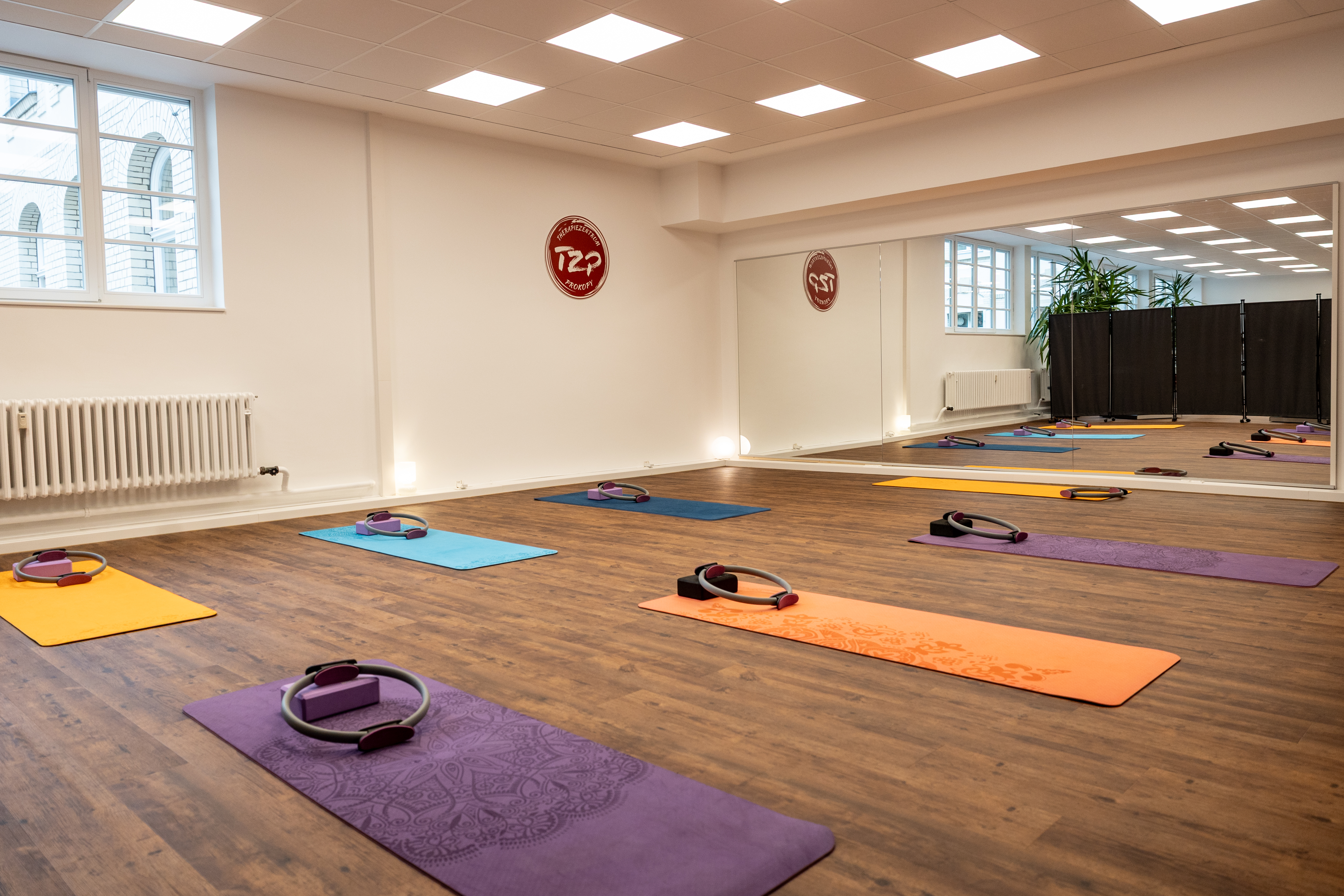 Mehrere bunte Yogamatten liegen in einem hellen Raum mit Spiegel und Fenstern