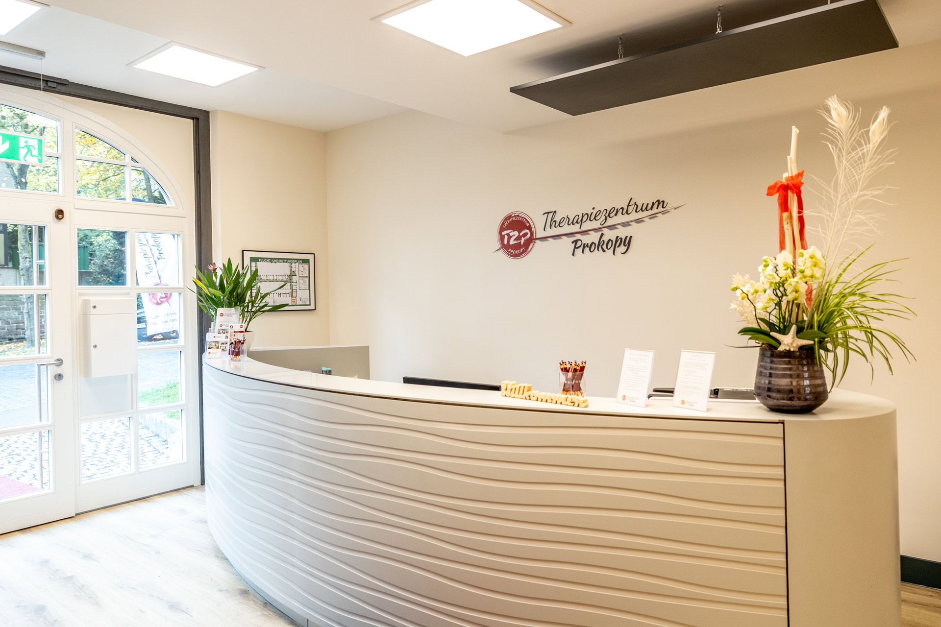 Heller Empfangsbereich mit geschwungener Theke und großer Blumenvase in Braun
